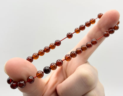 Hand holding a stretchy string of deep reddish-orange gemstone beads against a white background